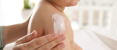 Baby wird auf der Schulter eingecremt