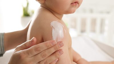 Baby wird auf der Schulter eingecremt