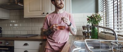 Mann lehnt sich in der Küche an, hat eine Tasse Tee in der Hand und schaut aus dem Fenster