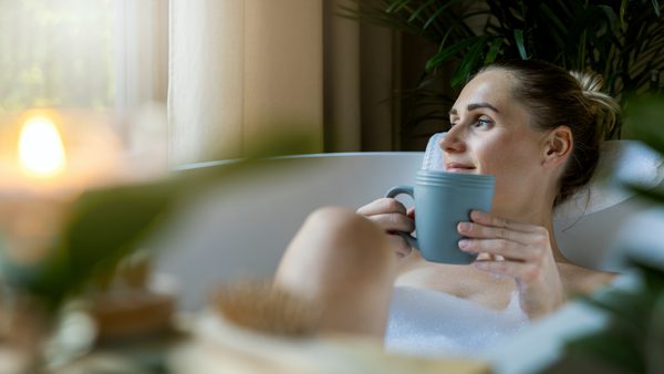 Frau liegt in der Badewanne mit einer Teetasse in der Hand gegen Übelkeit.