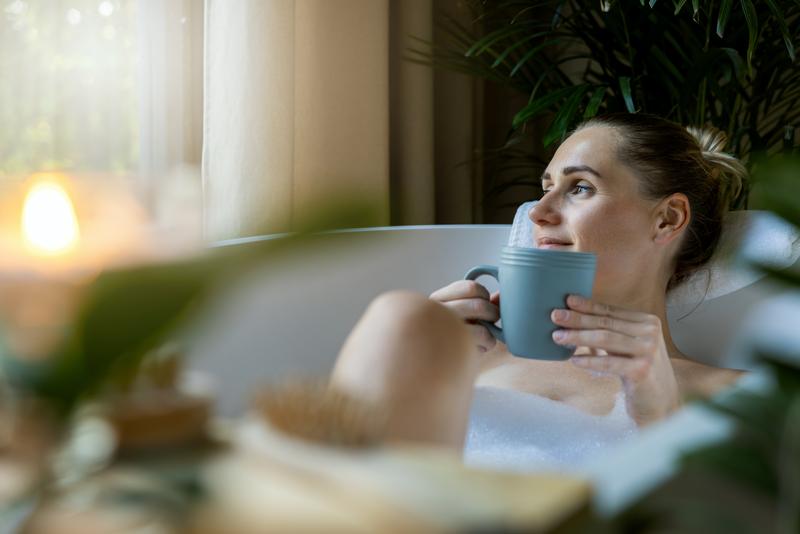 Frau liegt in der Badewanne mit einer Tasse in der Hand