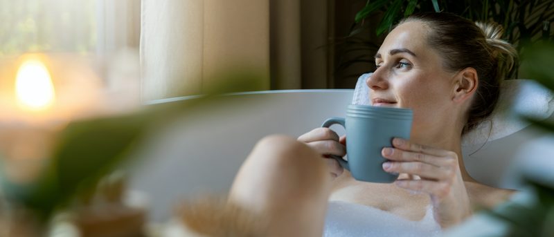 Frau liegt in der Badewanne mit einer Tasse in der Hand