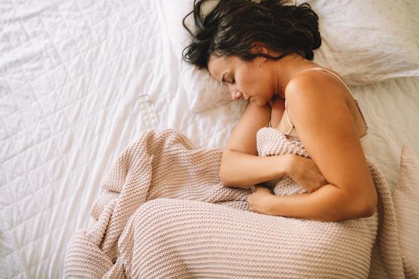Frau liegt im Bett und hat die Arme über dem Bauch