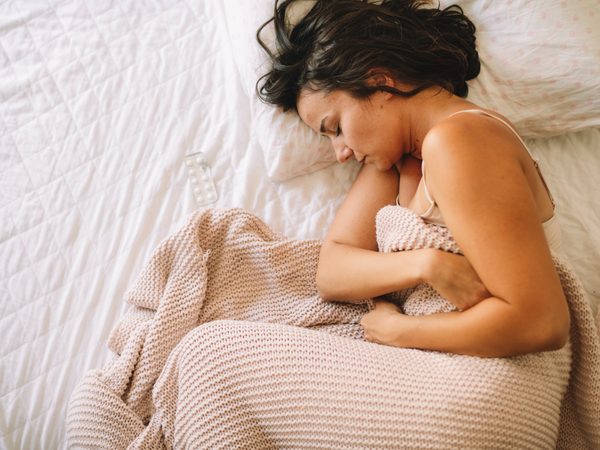 Frau liegt im Bett und hat die Arme über dem Bauch