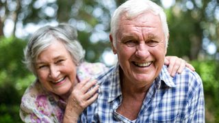 Älteres Paar im Grünen lacht in die Kamera.