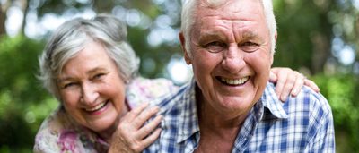 Älteres Paar im Grünen lacht in die Kamera.