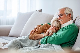 Frau mit Erkältung liegt mit Mann auf der Couch.