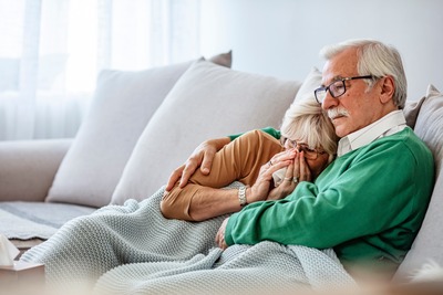 Frau mit Erkältung liegt mit Mann auf der Couch.