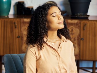 Junge Frau sitzt im Schneidersitz auf einem Stuhl im Wohnzimmer