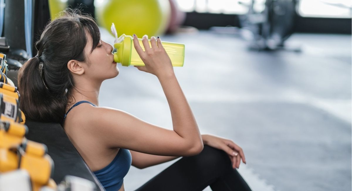 Frau beim Sport trinkt einen Shake.