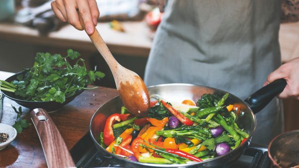 Frau bereitet verschiedenes Gemüse in Pfanne zu.