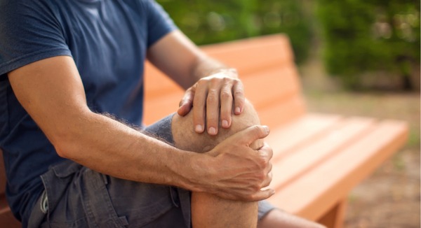 Mann sitzt auf Parkbank und hält schmerzendes Knie.
