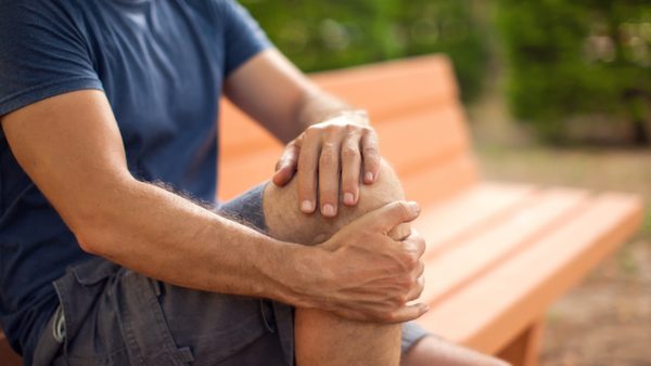 Mann sitzt auf Parkbank und hält schmerzendes Knie.