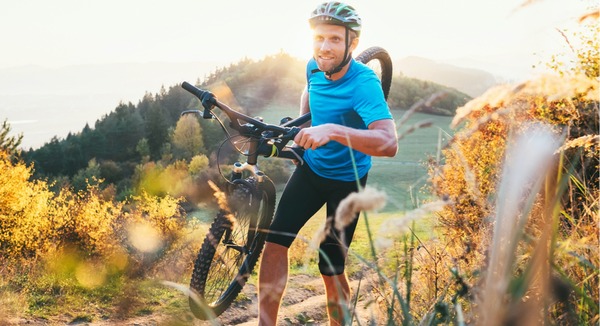 Mann in Sportkleidung trägt Mountainbike einen Berg hoch.