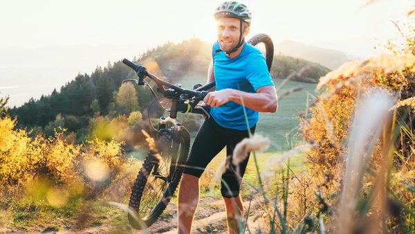 Mann in Sportkleidung trägt Mountainbike einen Berg hoch.