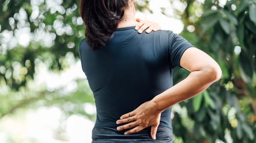 Frau in der Natur mit Händen an unteren Rücken