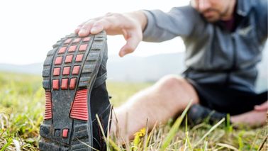 Mann sitzt auf dem Rasen und dehnt seine Wade