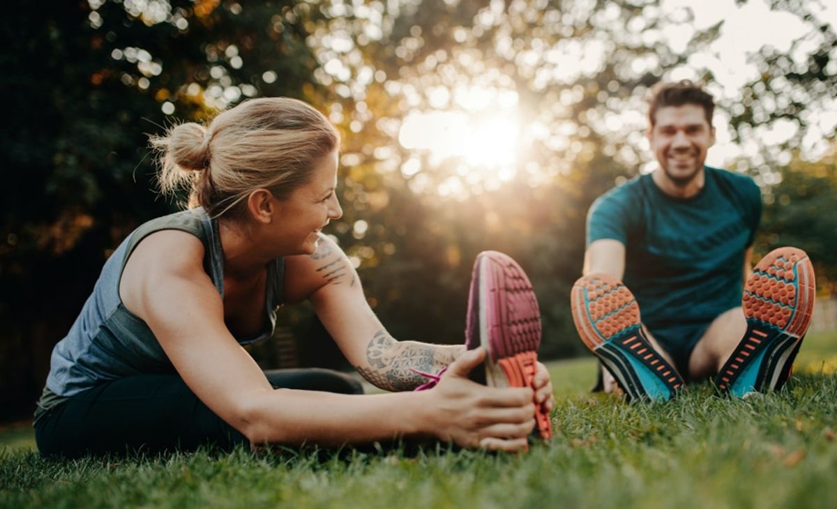 Mann und Frau machen Dehnübungen im Park als Regeneration nach dem Sport.