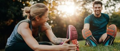 Mann und Frau machen Dehnübungen im Park als Regeneration nach dem Sport.