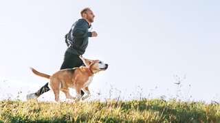 Mann joggt mit seinem Hund über eine Wiese