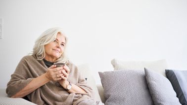 Frau mit Tasse in der Hand sitzt nachdenklich auf Sofa