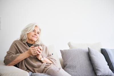 Frau mit Tasse in der Hand sitzt nachdenklich auf Sofa