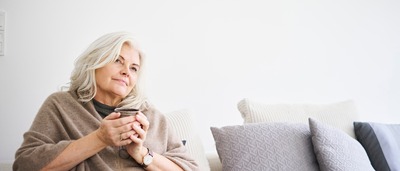 Frau mit Tasse in der Hand sitzt nachdenklich auf Sofa