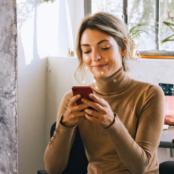Zittende vrouw kijkt en lacht naar telefoon in hand