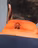 Close-up of a man’s back wearing an orange and navy jacket with embroidery featuring a semi-circle and “06” symbol on the collar.