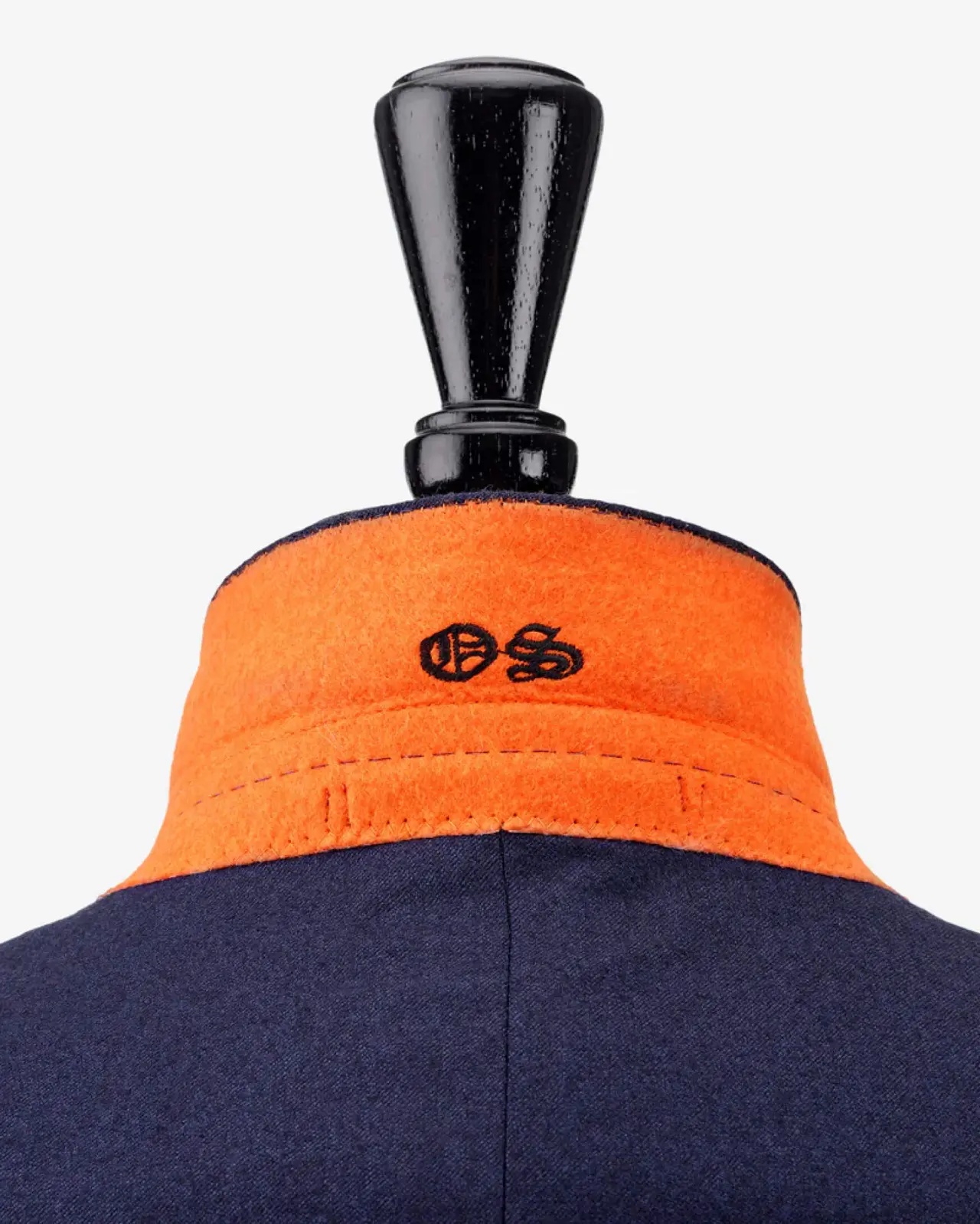 Close-up of a navy jacket with an orange collar and black OS emblem, displayed on a stand with a black top against a white background.