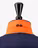 Close-up of a navy jacket with an orange collar and black OS emblem, displayed on a stand with a black top against a white background.