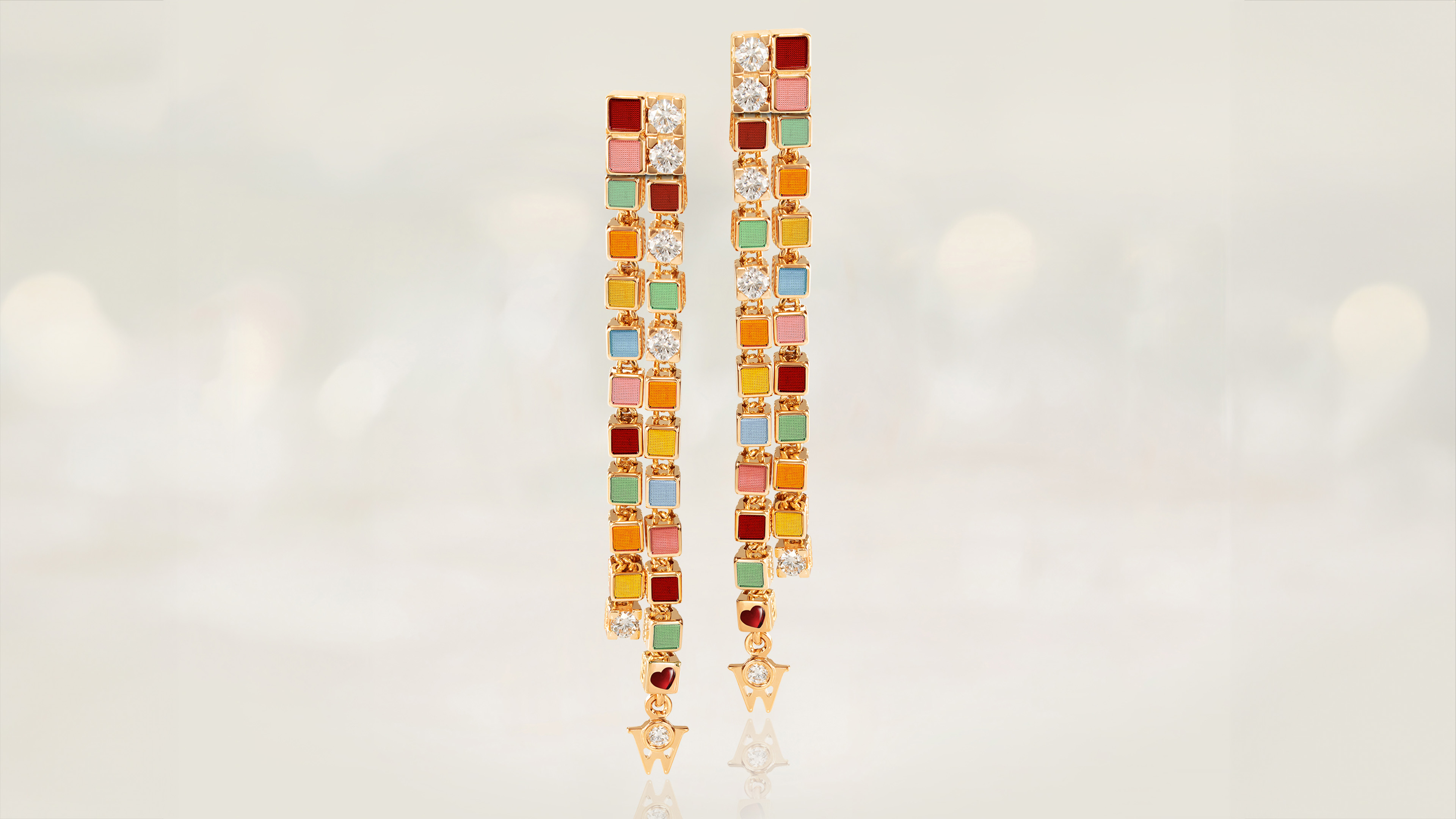 Die Farben des Regenbogens in 18-karätigem Gold. Die Ohrringe REGENBOGENVERFÜHRUNG können als Ohrhänger oder Ohrstecker getragen werden. Auf grauem Mood Hintergrund.