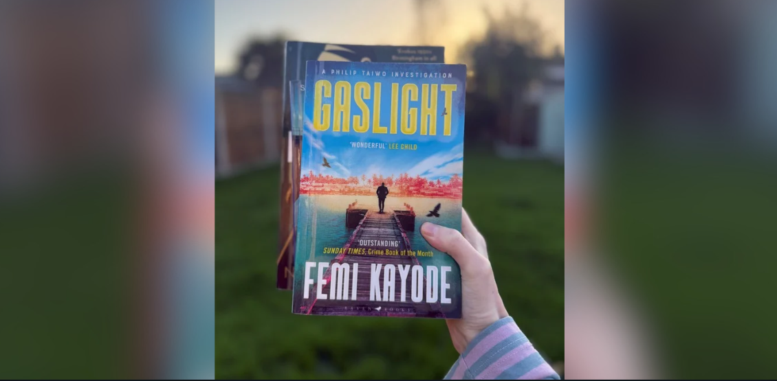 Person holding the book "Gaslight" by Femi Kayode, featuring a dock scene on the cover, with a blurred garden background.