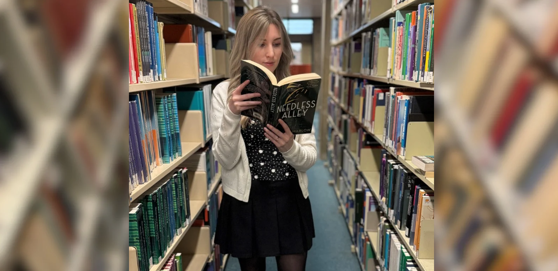 A woman stands between library shelves, reading a book titled "Endless Alley"