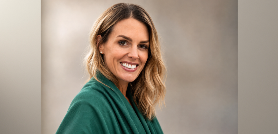 A woman with blonde hair and a green shawl smiles in her professional headshot