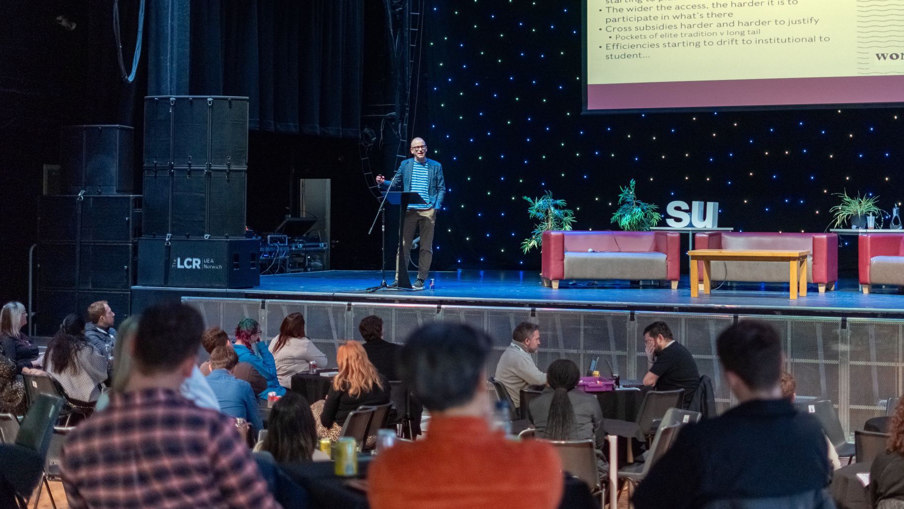 A person speaking on stage at the LCR.