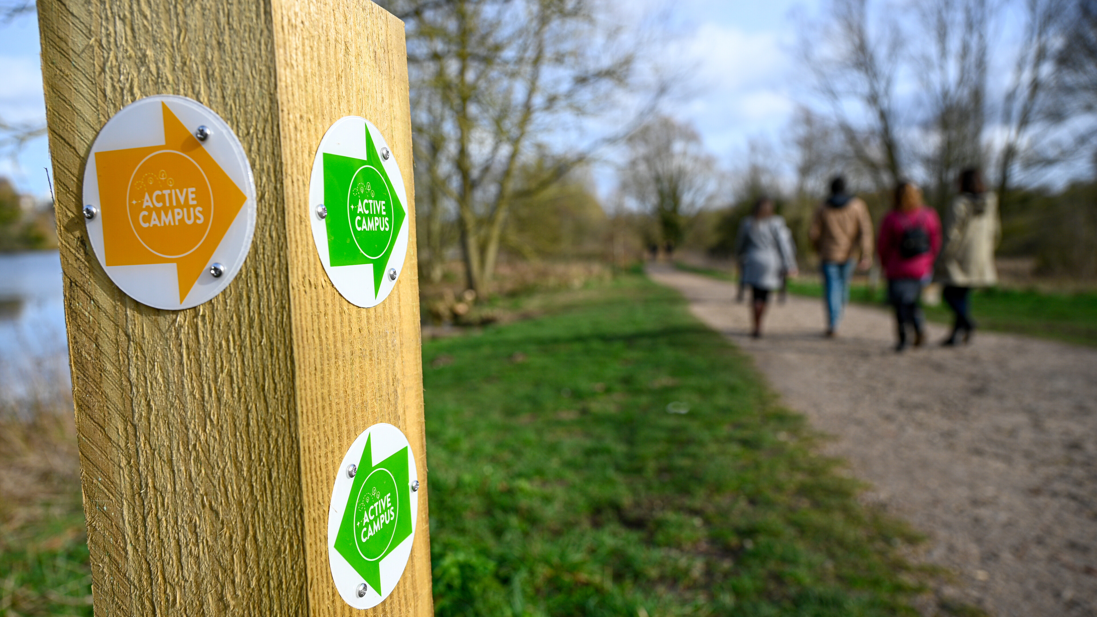 People walking past an Active Campus signpost near the Broad