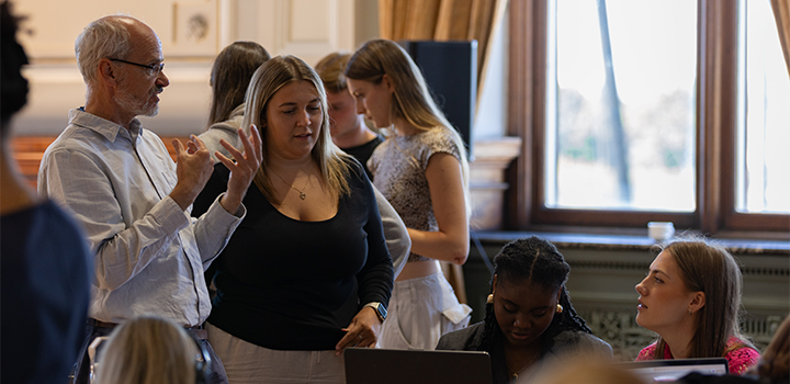 Two people standing on the left, one gesturing emphatically, while talking to two other people who are seated