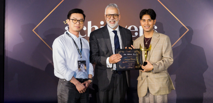 Three men at an award ceremony, with one in the centre holding a certificate and trophy.