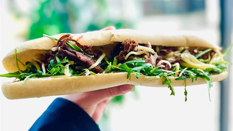 A hand holding a large filled baguette.