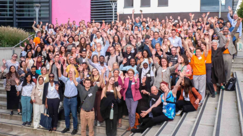 A large group of people gathered on outdoor steps, smiling and waving at the camera.