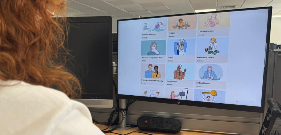 A woman looking at a computer screen for the Norfolk Family Courts website. The website on screen shows illustrated tiles on topics like divorce and child maintenance.