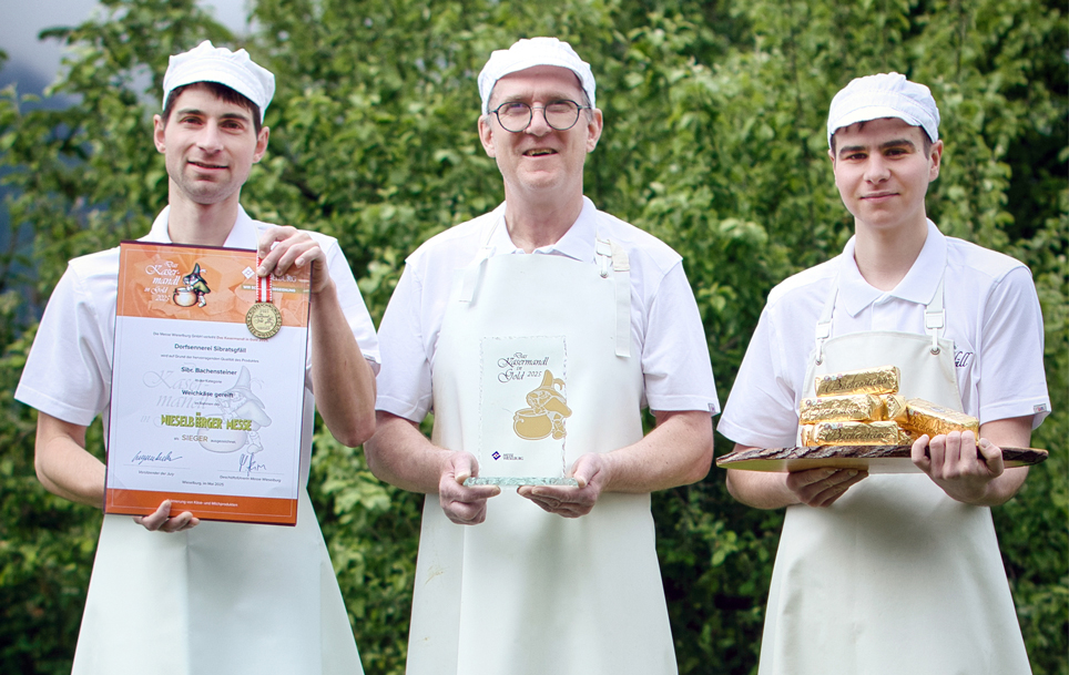 Die drei Senner präsentieren stolz die Auszeichnungen und die prämierten Produkte im Freien, im Hintergrund Grün.