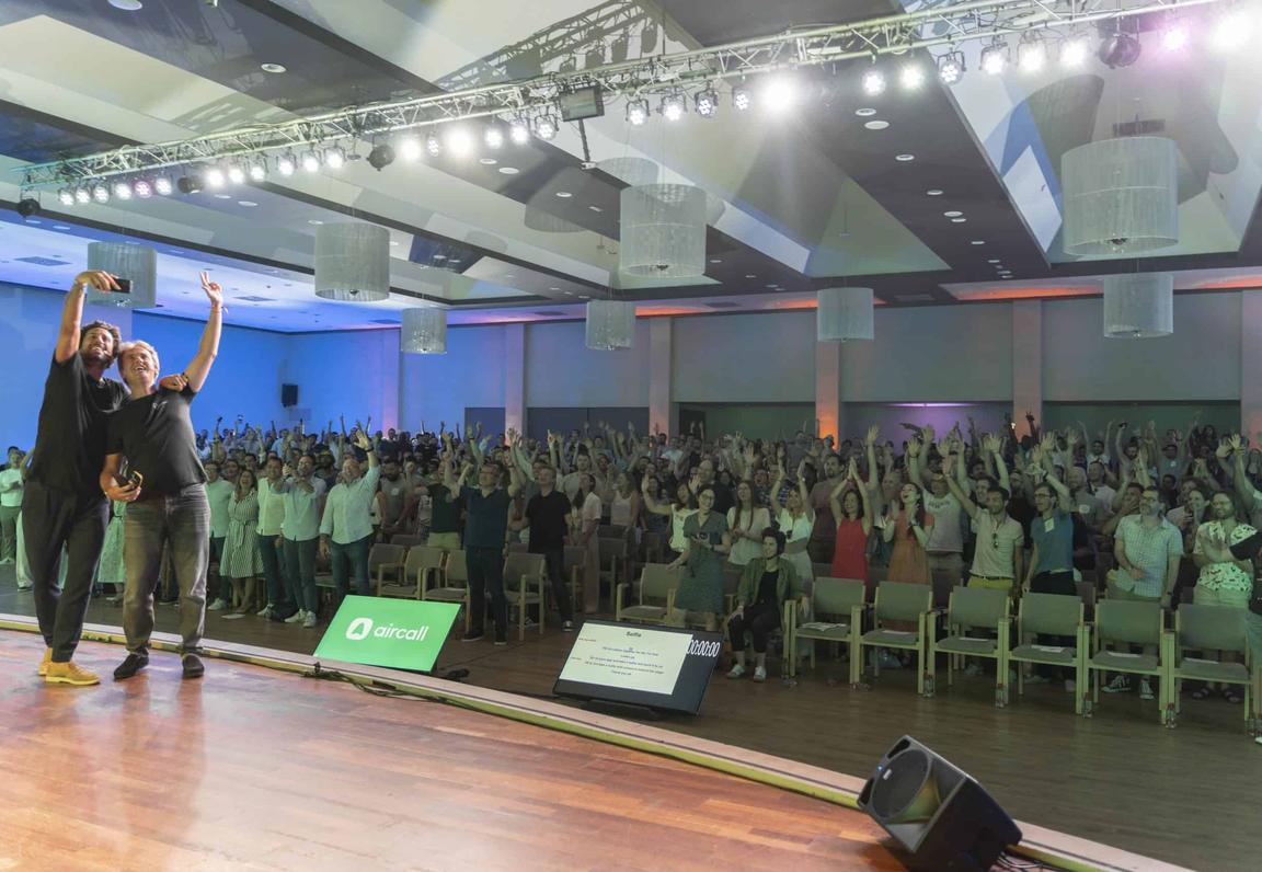 Group photo from Aircall's 2022 Company Offsite, featuring co-founder Olivier and Jonathan taking a selfie on stage