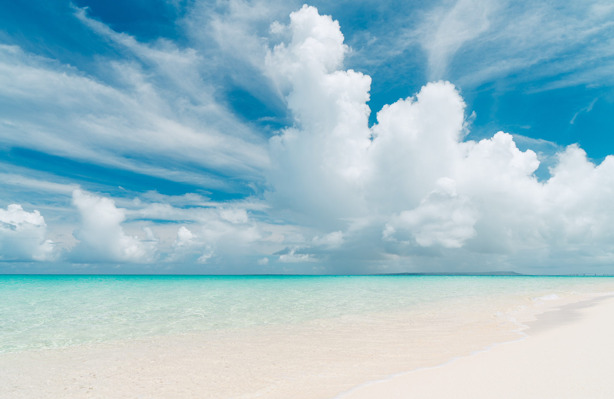Crystalline turquoise sea with some clouds and white sand