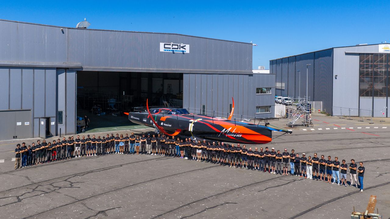 Team Malizia and the CDK team standing in front of the boat on 3 July 2026 in Lorient