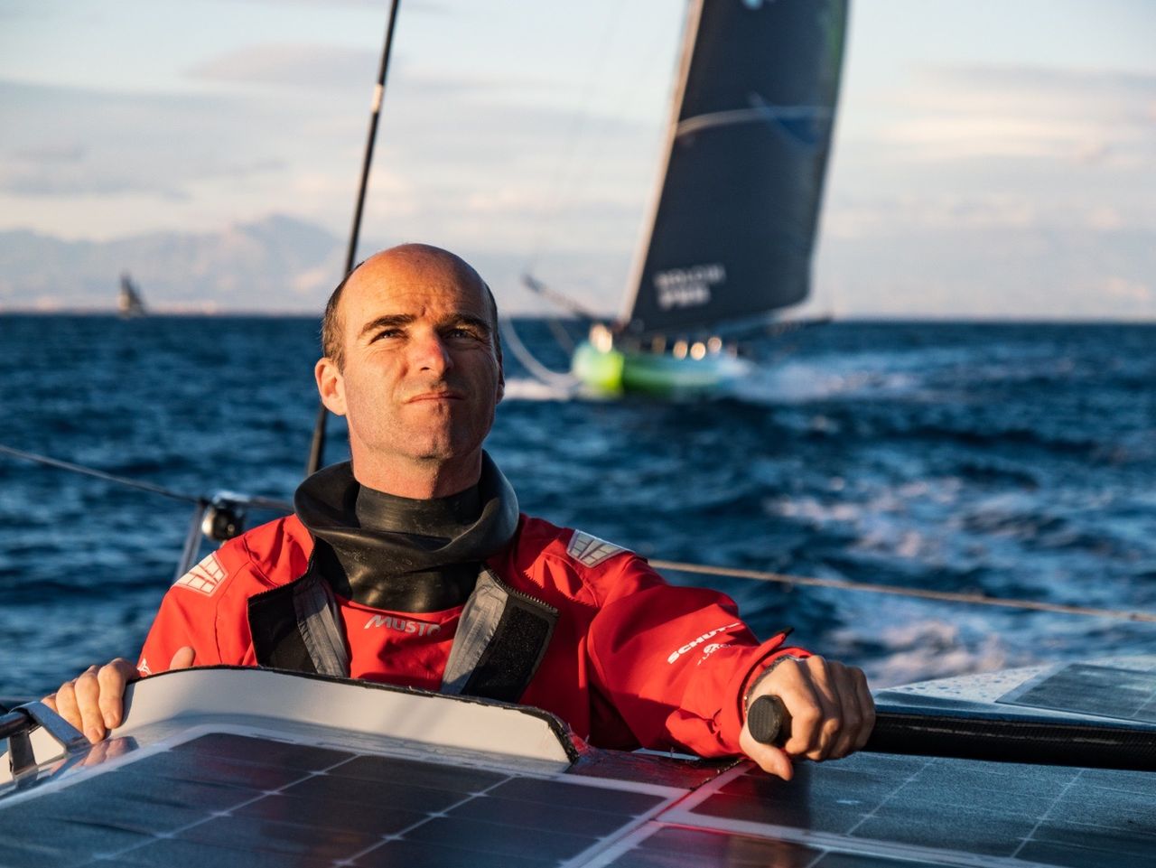 A very experienced co-skipper Nico Lunven steering the boat by hand shortly after the start, with Team Holcim-PRB and the Spanish coast in the background.