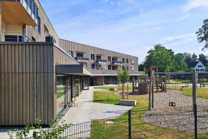 Holzverkleidetes Gebäude mit Balkonen, Terrasse und Spielplatz im sonnigen Innenhof