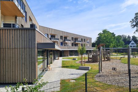 Holzverkleidetes Gebäude mit Balkonen, Terrasse und Spielplatz im sonnigen Innenhof
