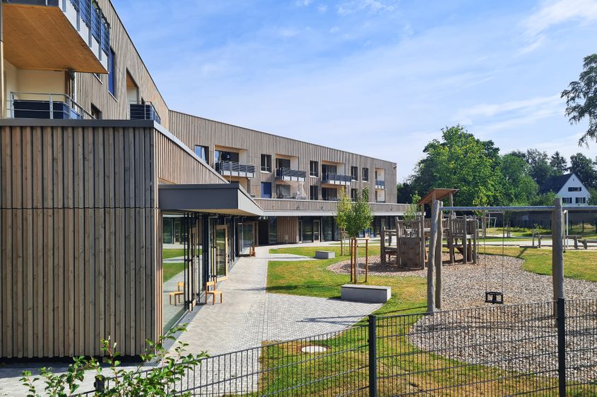 Holzverkleidetes Gebäude mit Balkonen, Terrasse und Spielplatz im sonnigen Innenhof